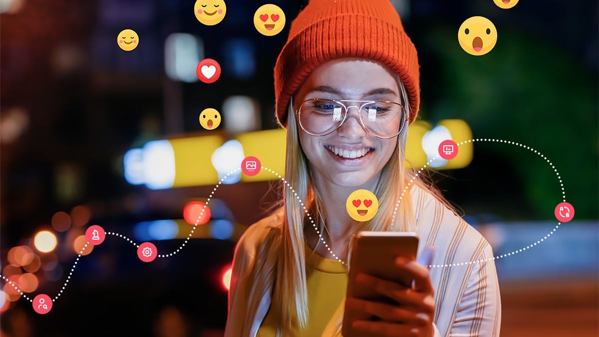 lächelnde, blonde Person mit orangener Mütze schaut auf Instagram ihres Smartphones, davor angedeutete Schritte zur Schaltung von Ads. Im Hintergrund Emoticons und Herzen